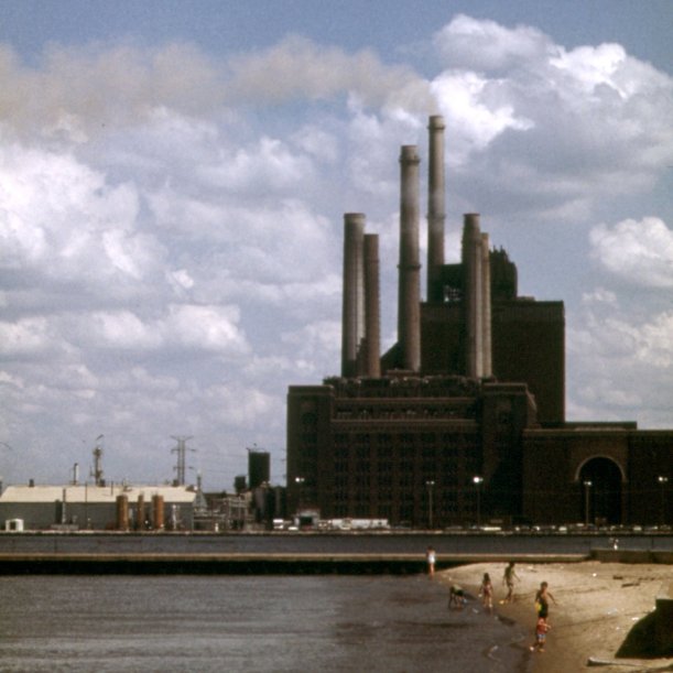 A coal fired plant, with big smokestacks, and a lake and beach in the foreground