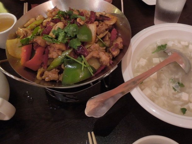 A bowl of Sichuan dry pot, with mixed vegetables and chicken in a metal bowl, and a white bowl of seafood tofu soup
